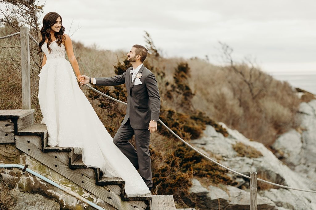 Bride holding Groom's hand leading him up staircase on the rocky cliffside
