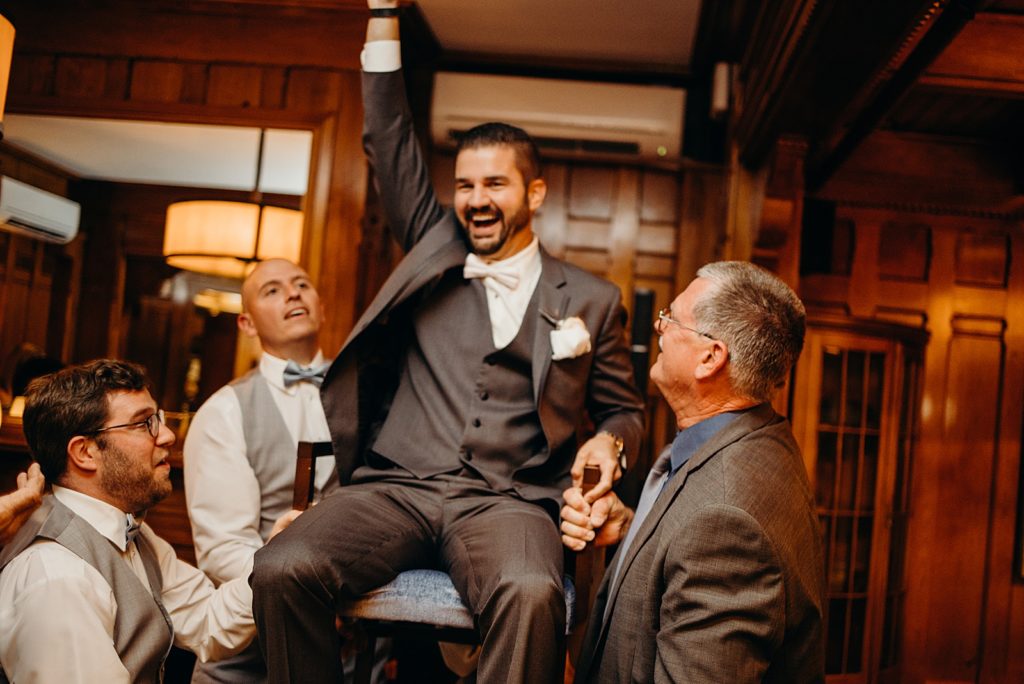 Groom being lifted up in chair by family during Reception