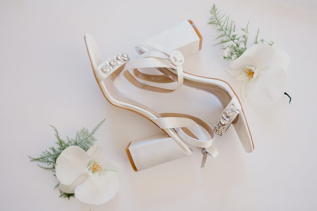 Detail shot of wedding heels with white flowers next to it