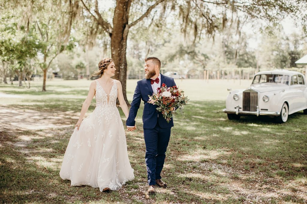 Groom holding bouquet and walking with Bride holding hands
