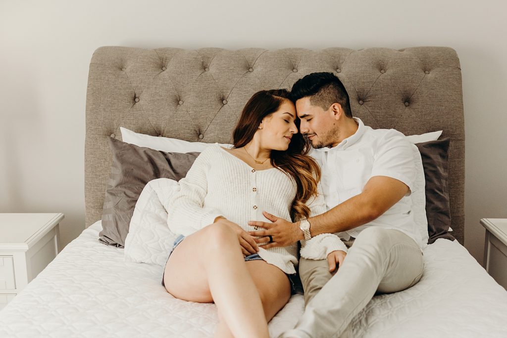 Pregnant couple laying in bed resting their heads on each other