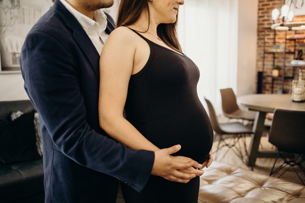 Closeup of Man holding woman's pregnant stomach from behind in living room