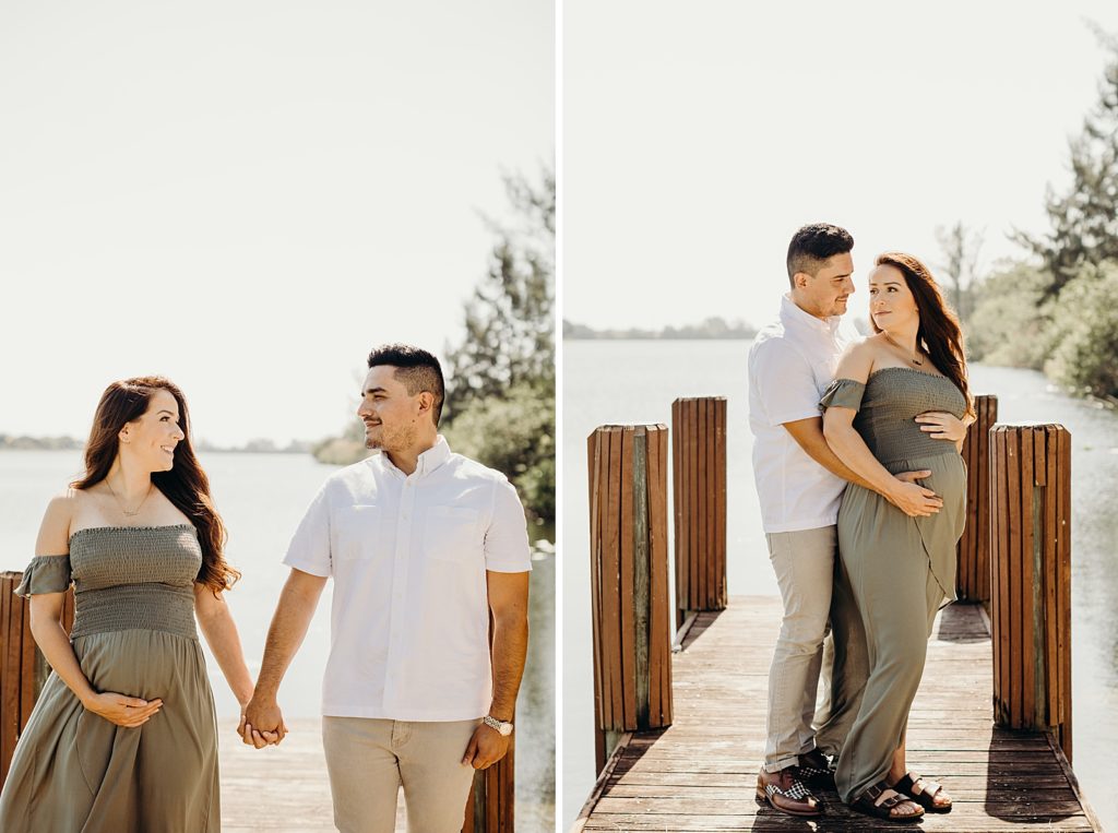 Couple holding hands and standing on small wooden dock with pregnant soon-to-be mother holding baby bump