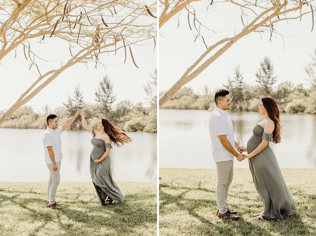 Pregnant soon-to-be Mother twirling while holding Man's hand up in the air next to body of calm water