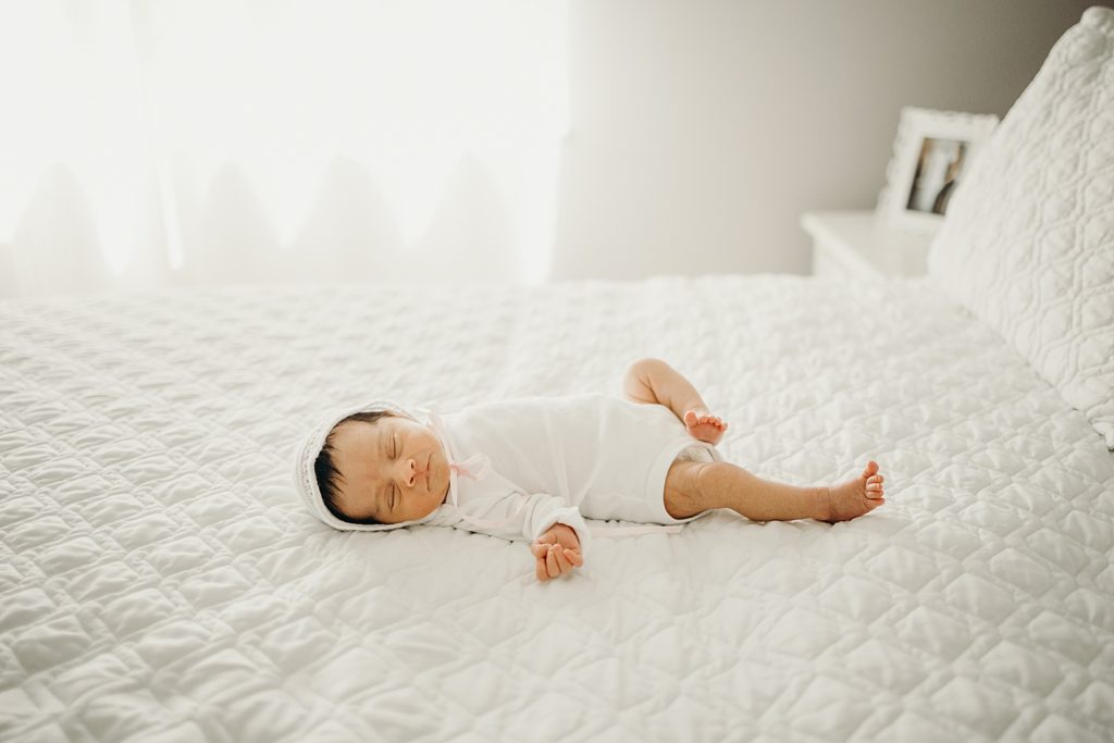 Baby in white onesie sleeping on parent's white bed
