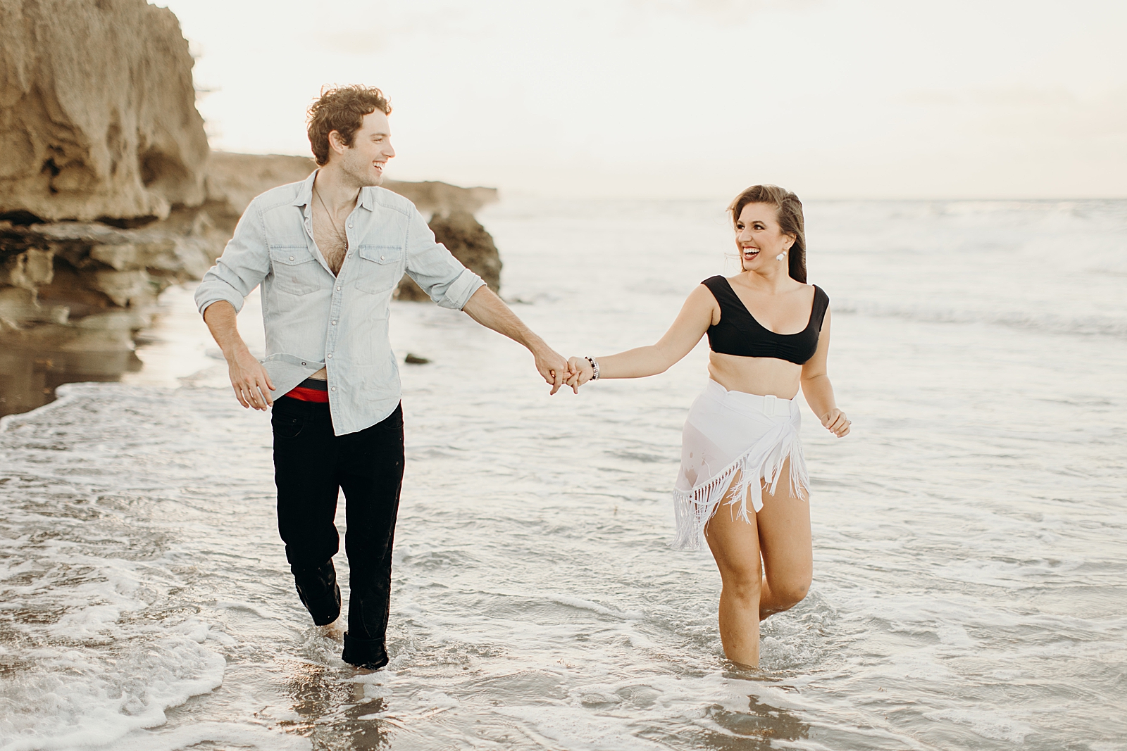 Couple extending arms to hold hands and looking at each other as they run through the water