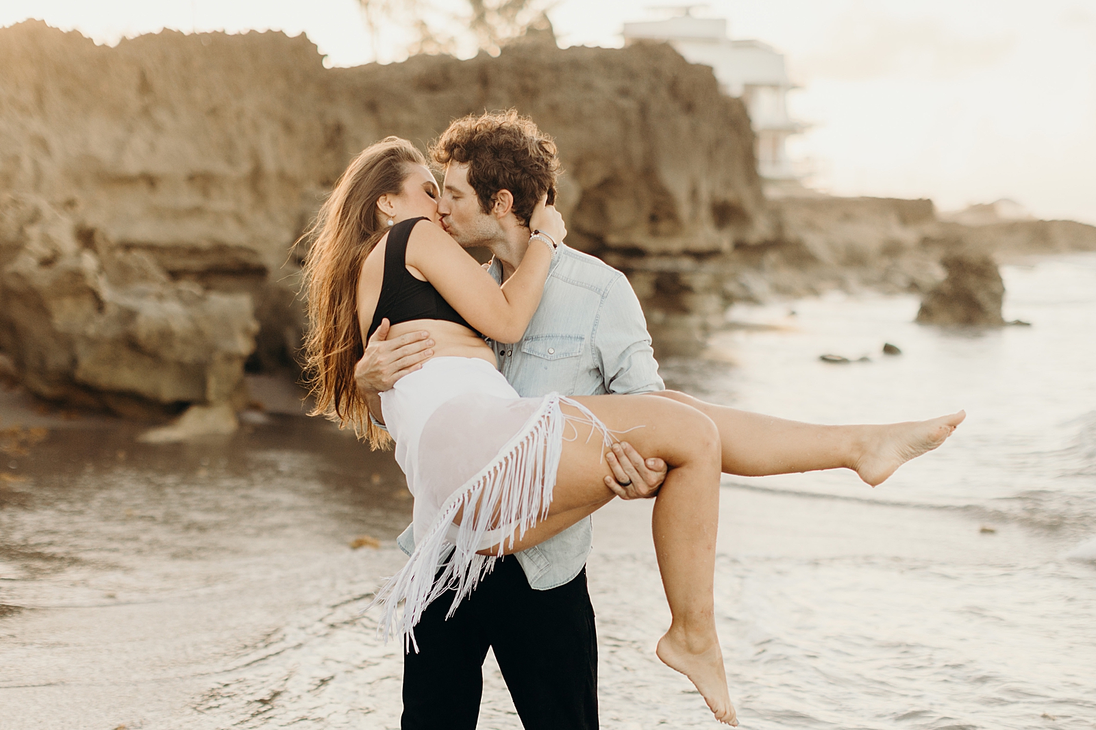 Man holding woman and kissing her with beach rocks behind them