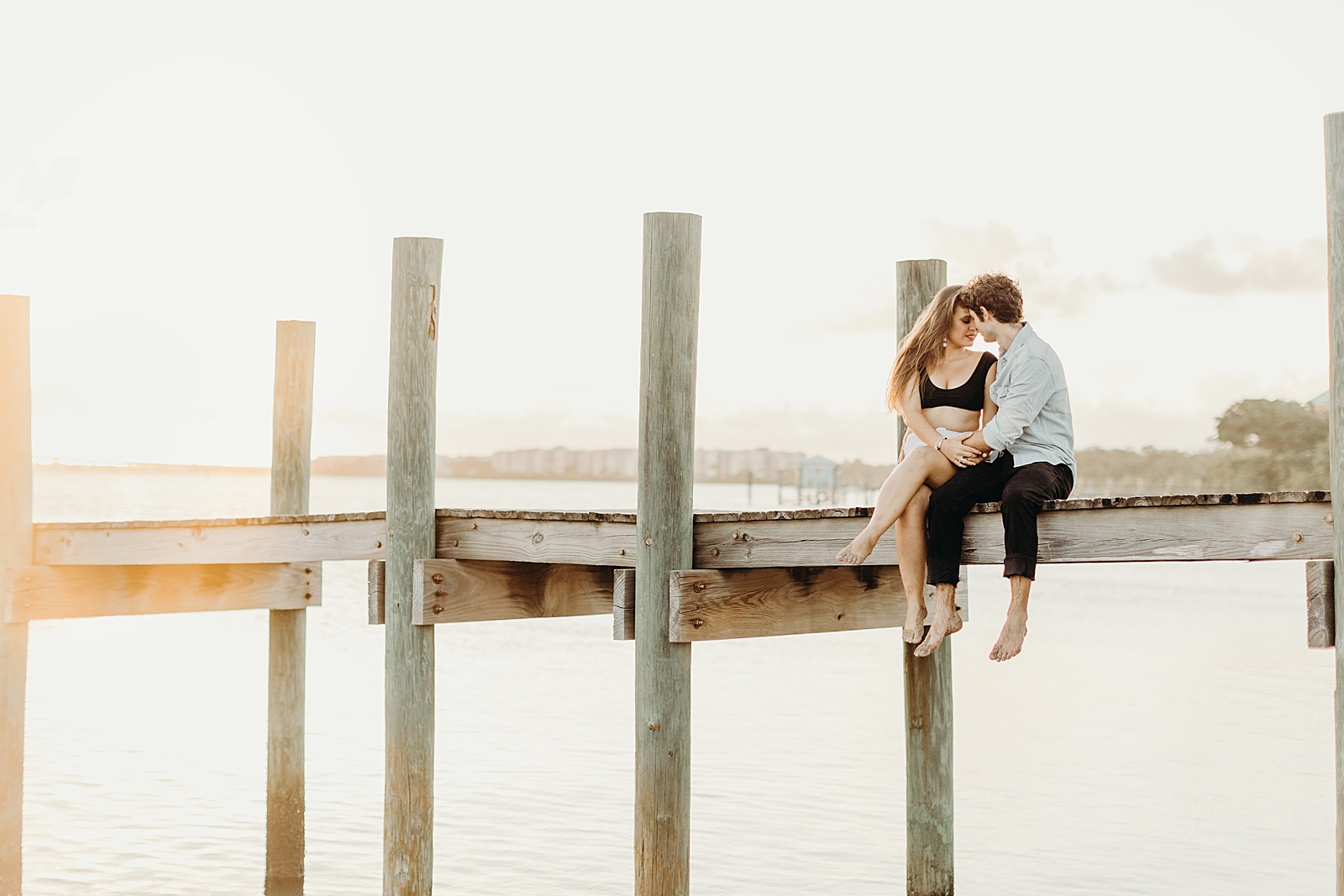 Couple sitting on wooden beach pier with legs dangling 