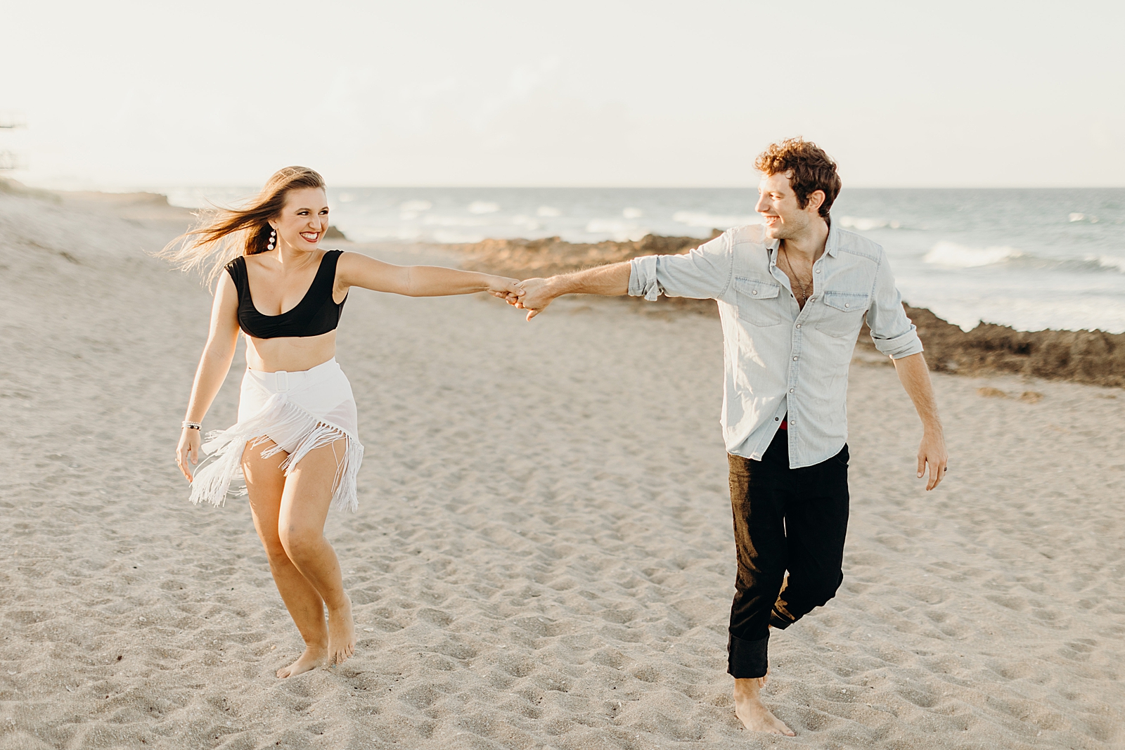 Couple extending their arms out and holding hands while walking barefoot on the sand of the beach