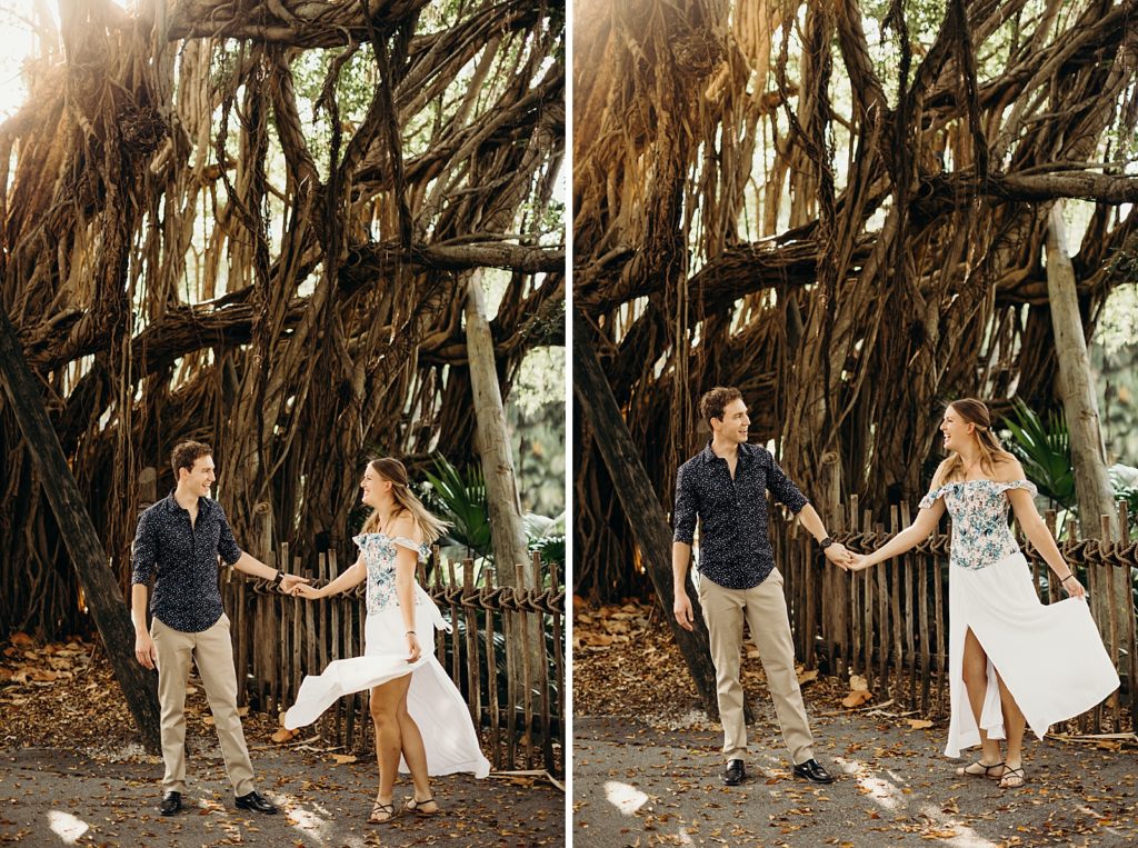 Couple holding hands and looking at each other with woman twirling dress in front of banyan tree