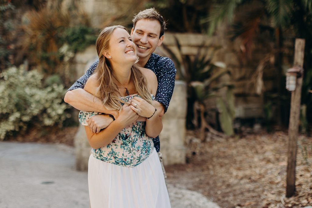 Man hugging woman from behind in overgrown botanical area