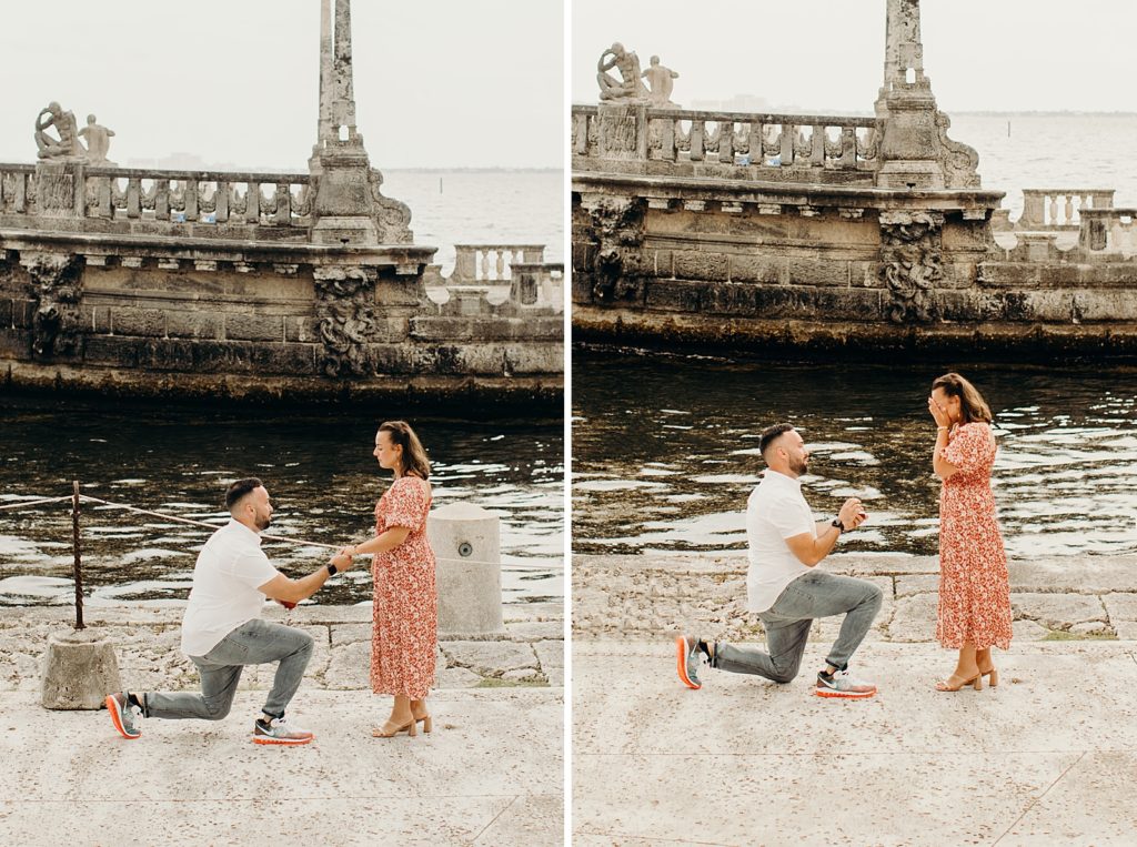 Man on one knee proposing to woman in front of water and rundown columns