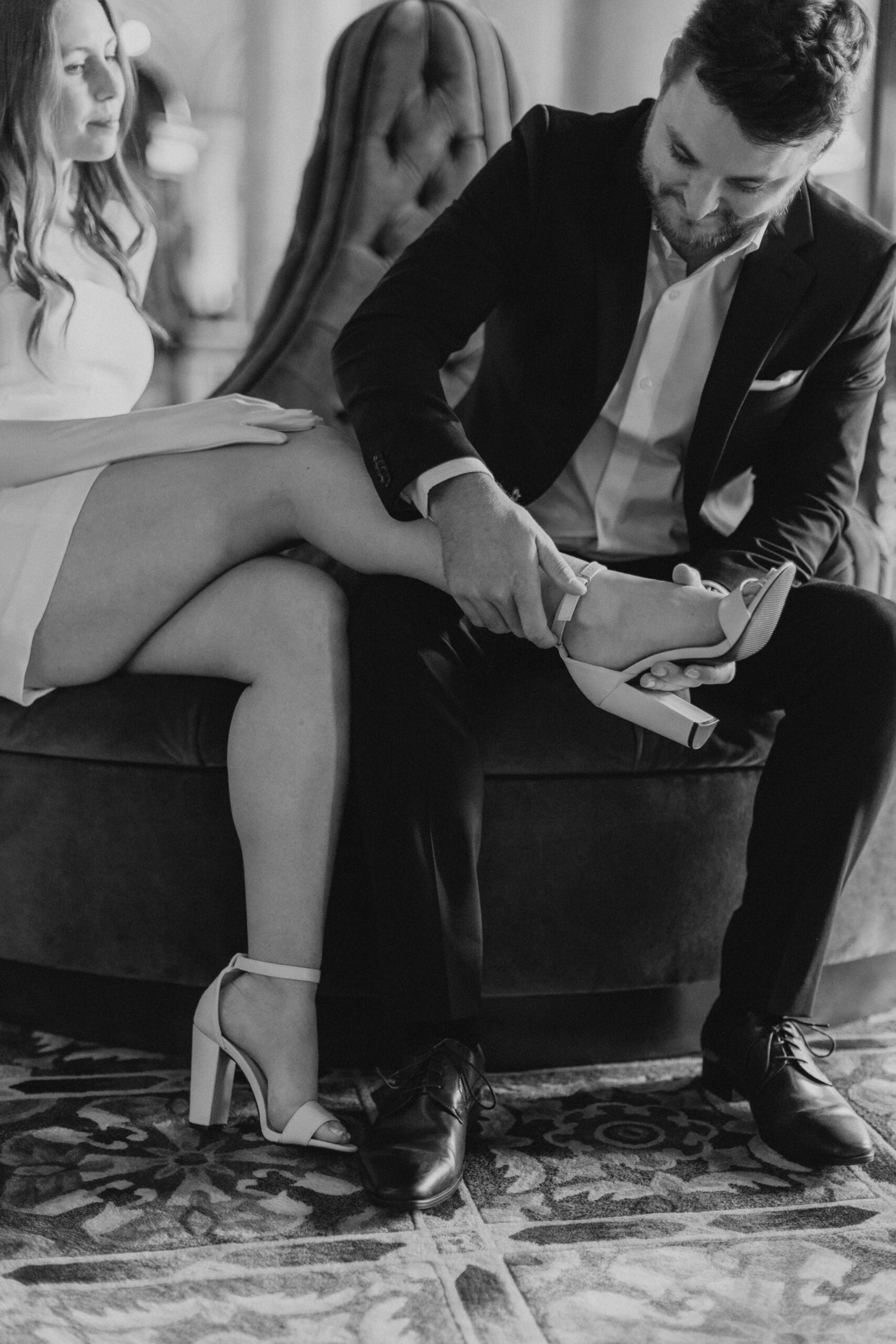 Groom helping bride put on shoes inside Biltmore Hotel, showing how to look natural in wedding photos.